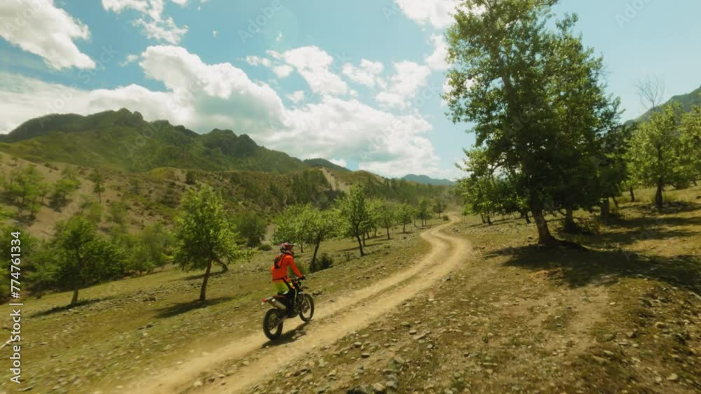 Man stands riding motorcycle across young wood fpv. Trained biker in red jacket maneuvers motorbike travelling at highland countryside. Motocross lifestyle Man stands riding motorcycle across young wood fpv. Trained biker in red jacket maneuvers motorbike travelling at highland countryside. Motocross lifestyle