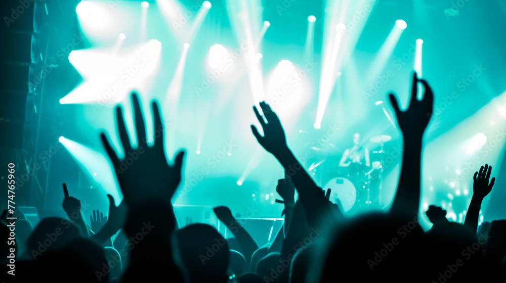 Concert crowd with raised hands, stage lights, live music event.
