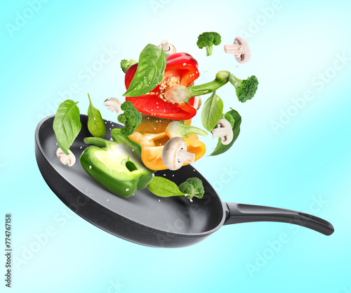 Frying pan with fresh ingredients in air on light blue background