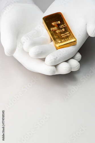 Trading of gold bars.  Hands in glove holding gold bar against grey background with free place for text.