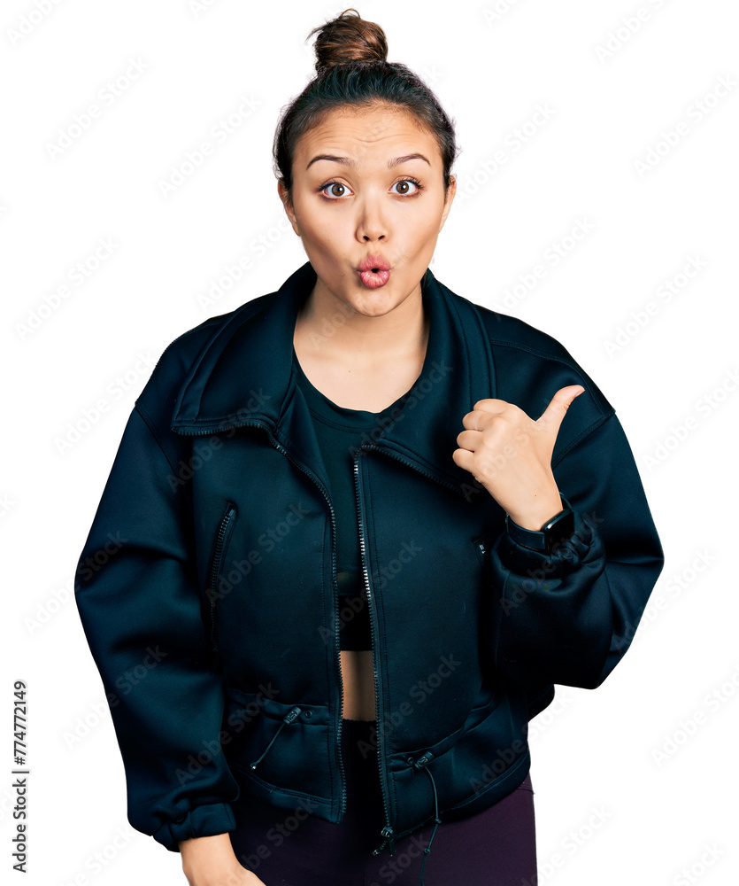 Young hispanic girl wearing sportswear surprised pointing with hand finger to the side, open mouth amazed expression. Young hispanic girl wearing sportswear surprised pointing with hand finger to the side, open mouth amazed expression.