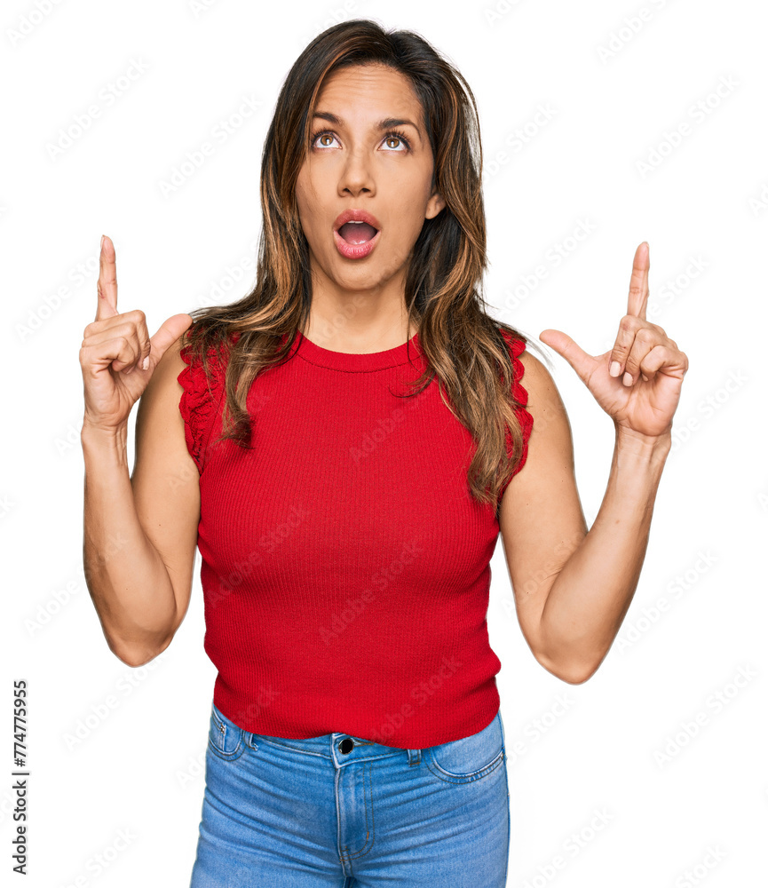 Young hispanic woman wearing casual clothes amazed and surprised looking up and pointing with fingers and raised arms. Young hispanic woman wearing casual clothes amazed and surprised looking up and pointing with fingers and raised arms.