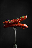 Hot Bavarian sausages with ketchup and thyme on a fork. On a black background.