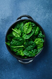 Spinach leaves in a black stone plate on a dark background. Top view.