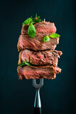 Slices of ribeye steak on a metal fork. Roast medium rare. On a black background.