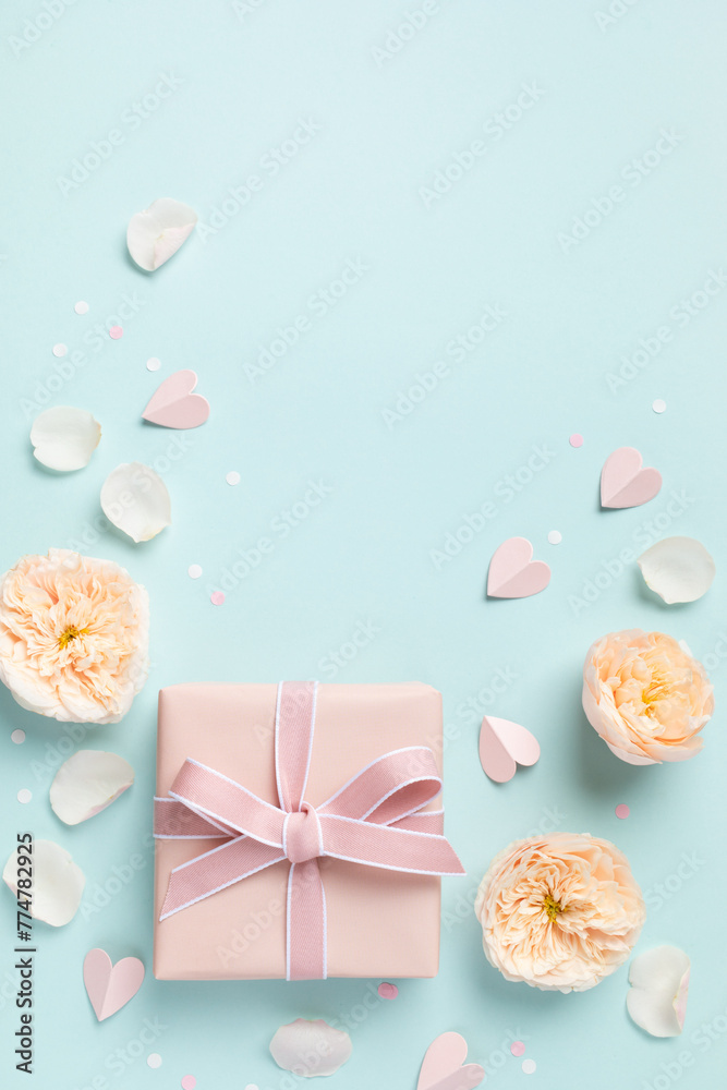 Fototapeta premium Lovely greeting card for Birthday, Woman or Mothers Day. Pink hearts, rose flowers and gift box on blue pastel table top view. Flat lay.