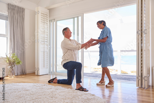 Mature Couple With Man Proposing Marriage Kneeling And Giving Woman Ring In Beach Front Property photo