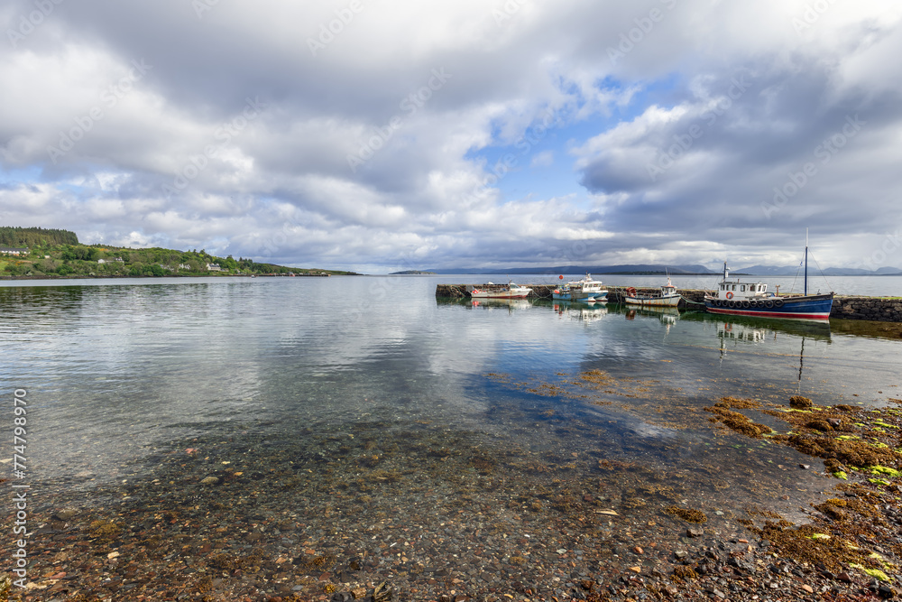 Morning light bathes the peaceful harbor of Broadford, showcasing moored vessels and a crystal-clear sea meeting the pebbled shore. Scotland Morning light bathes the peaceful harbor of Broadford, showcasing moored vessels and a crystal-clear sea meeting the pebbled shore. Scotland
