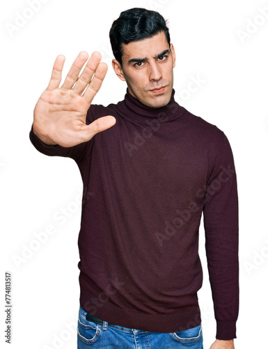 Handsome hispanic man wearing casual turtleneck sweater doing stop sing with palm of the hand. warning expression with negative and serious gesture on the face. © Krakenimages.com