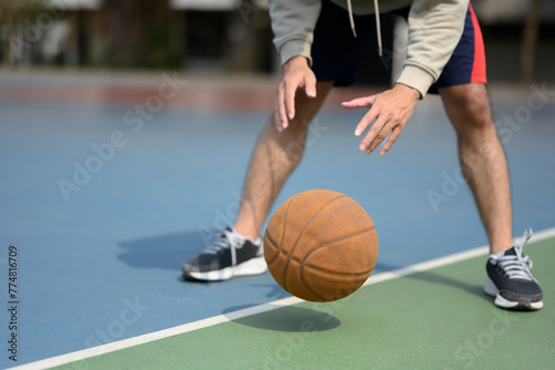Cropped shot of sporty man bouncing ball in an urban court. Sport and active lifestyle concept © Prathankarnpap