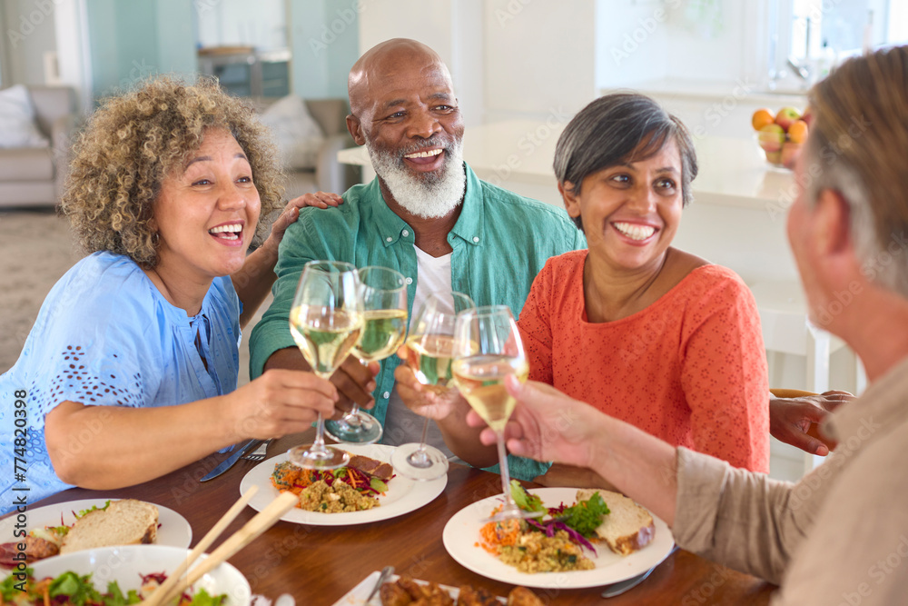 Group Of Smiling Mature Friends At Home Sitting Around Table Meeting For Lunch And Wine Together Group Of Smiling Mature Friends At Home Sitting Around Table Meeting For Lunch And Wine Together