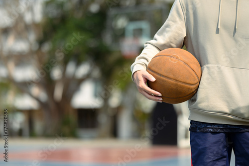 Teenage man holding a ball standing on the basketball court. Sport and active lifestyle concept