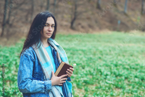 Young woman with book on the walk. Time for reading. Reading book concept. Woman enjoying spring day at nature.