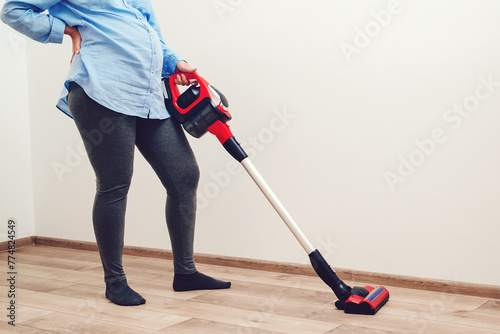 Easy cleaning with a wireless vacuum cleaner. Pregnant woman cleaning floor with handheld vacuum cleaner.