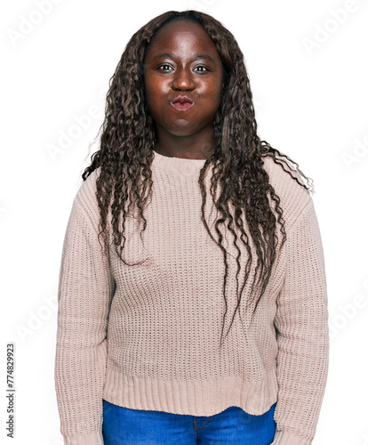Young african woman wearing wool winter sweater puffing cheeks with funny face. mouth inflated with air, crazy expression.