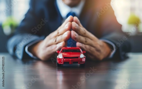 Businessman protect with his hands a red car on white table, concept for insurance, buying, renting, fuel or service and repair costs