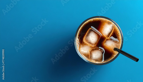 Glass of ice coffee on blue background, flat lay with copy space. Refreshing drink.