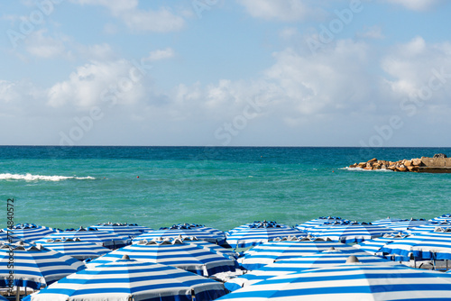 Fototapeta Naklejka Na Ścianę i Meble -  Striped colorful umbrellas and sun beds at Monterosso al Mare beach against turquoise sea 