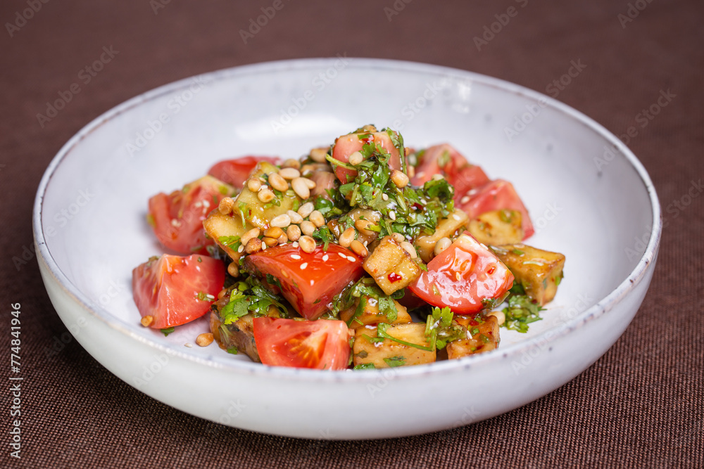Fresh tomato and avocado salad with pine nuts and herbs on a white plate Fresh tomato and avocado salad with pine nuts and herbs on a white plate