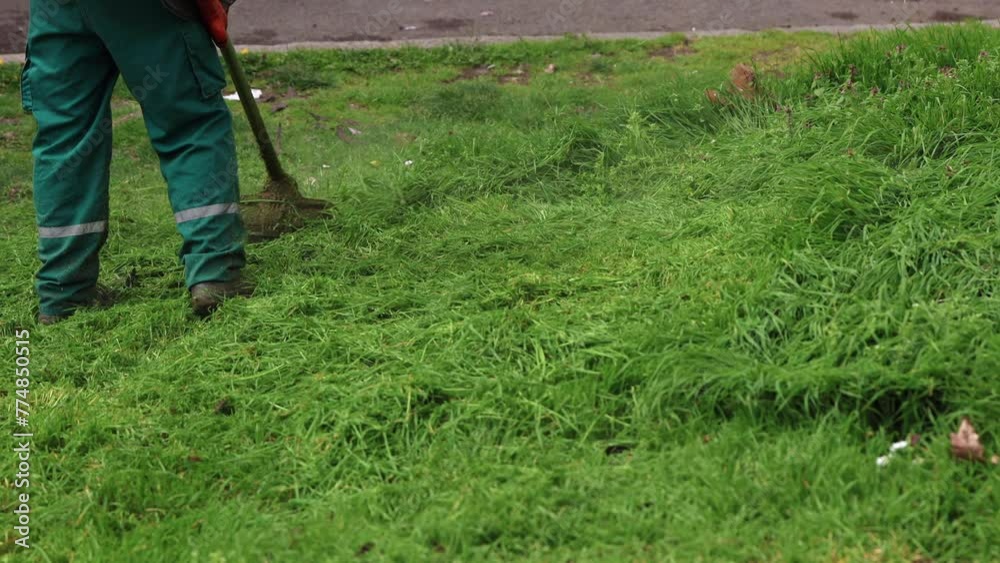 A professional maintenance worker in a green uniform efficiently uses a petrol weed trimmer to cut grass and dandelions in an urban park setting A professional maintenance worker in a green uniform efficiently uses a petrol weed trimmer to cut grass and dandelions in an urban park setting