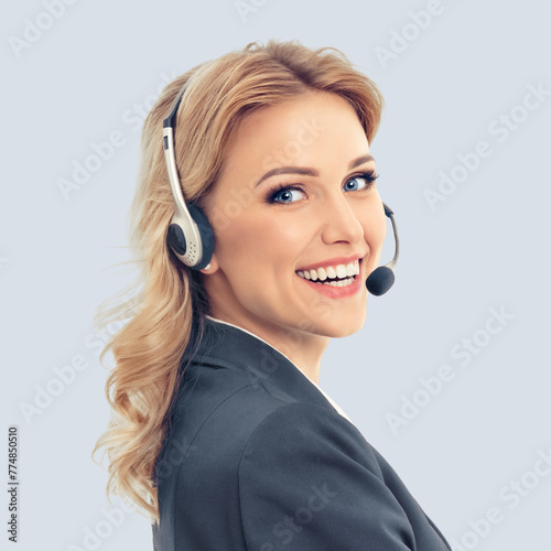 Call center. Smiling female support phone operator in headset, in grey confident suit, isolated over against gray background. Customer service help consulting. Square composition image.