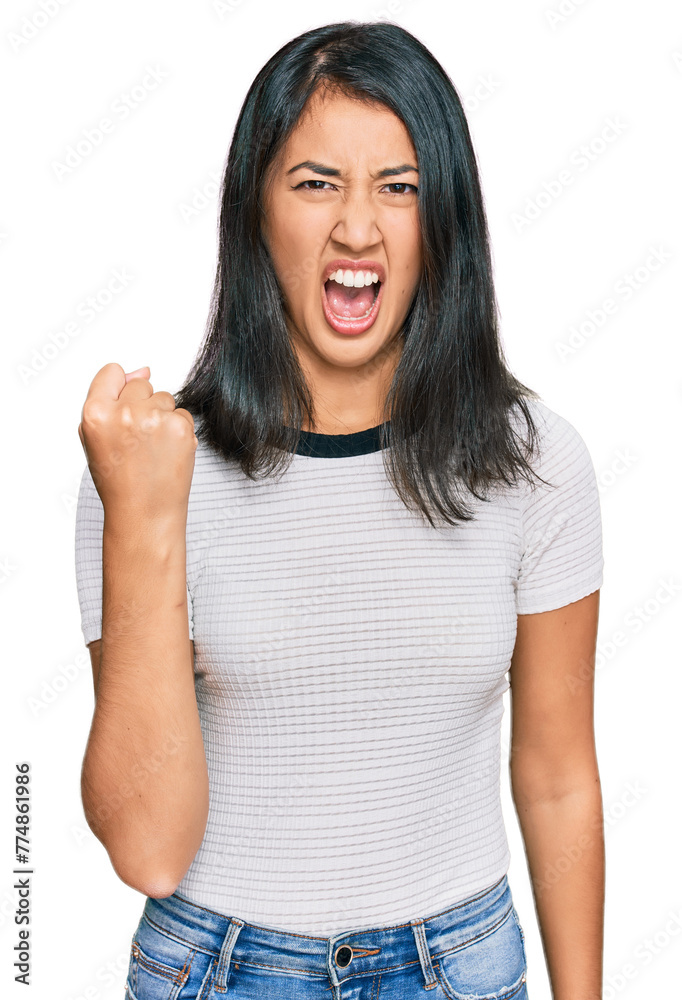 Beautiful asian young woman wearing casual white t shirt angry and mad raising fist frustrated and furious while shouting with anger. rage and aggressive concept.