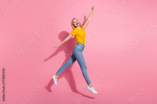 Full length photo of cute excited lady dressed yellow t-shirt jumping high having fun empty space isolated pink color background photo
