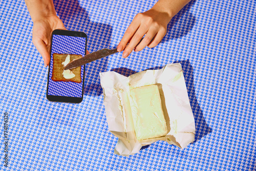 Hands buttering virtual toast on a smartphone screen with real butter and knife. Ad for a cooking app showcasing interactive and digital recipe tutorials. Concept of pop art photography, creativity photo