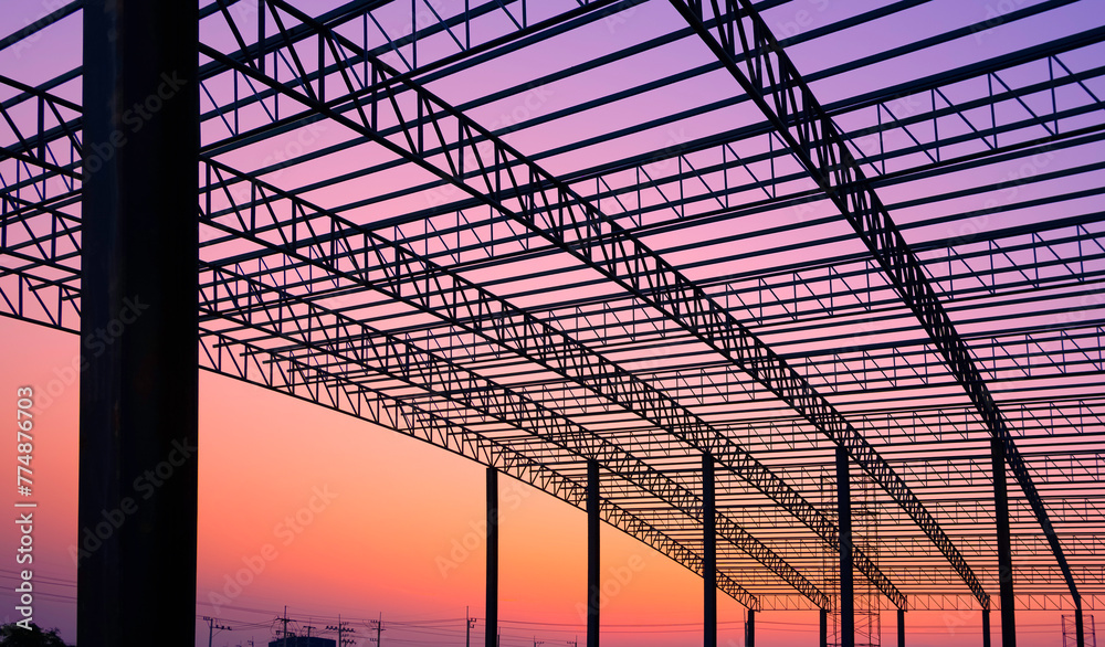 Silhouette of incomplete factory building structure with curve metal roof beam outline and column in construction site against sunset sky background, perspective and inside view Silhouette of incomplete factory building structure with curve metal roof beam outline and column in construction site against sunset sky background, perspective and inside view