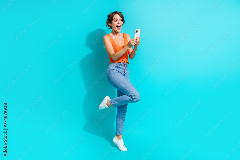 Full size photo of ecstatic nice girl dressed knitwear top denim pants astonished staring at smartphone isolated on blue color background Full size photo of ecstatic nice girl dressed knitwear top denim pants astonished staring at smartphone isolated on blue color background