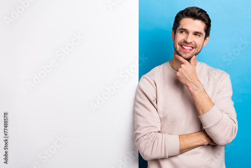 Photo of nice young man think look empty space placard wear beige sweatshirt isolated on blue color background