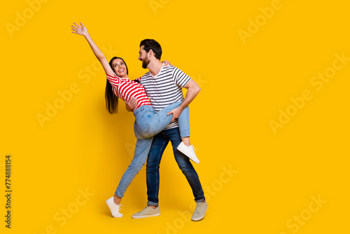Full size photo of gorgeous couple dressed striped t-shirt dancing together girl raising hand up isolated on yellow color background