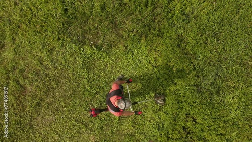 Aerial view of worker in protective clothing cutting grass with weed trimmer
