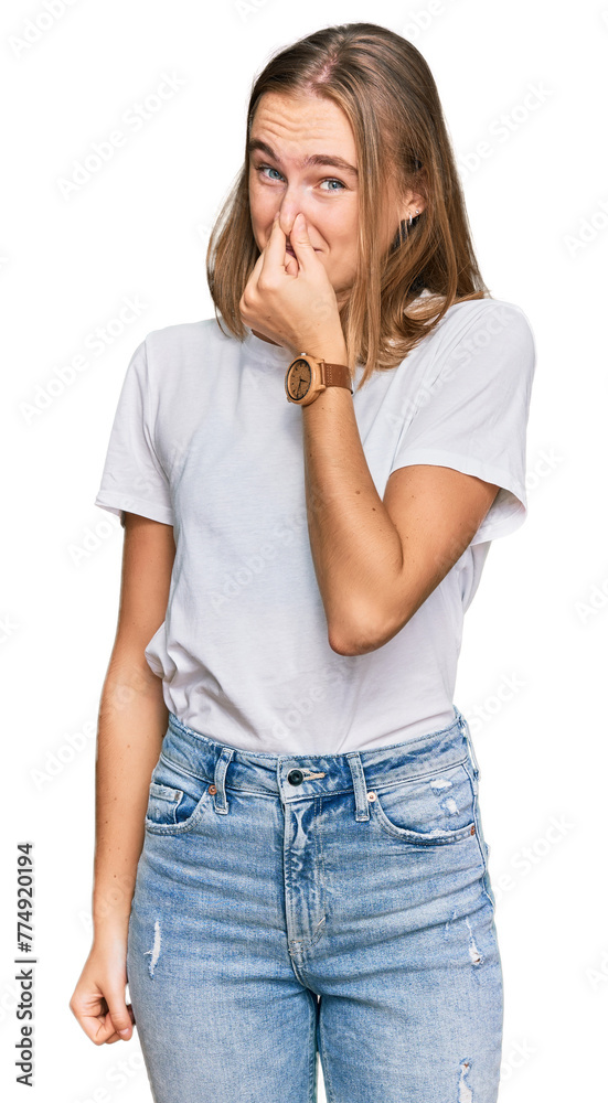 Beautiful young blonde woman wearing casual white t shirt smelling something stinky and disgusting, intolerable smell, holding breath with fingers on nose. bad smell Beautiful young blonde woman wearing casual white t shirt smelling something stinky and disgusting, intolerable smell, holding breath with fingers on nose. bad smell