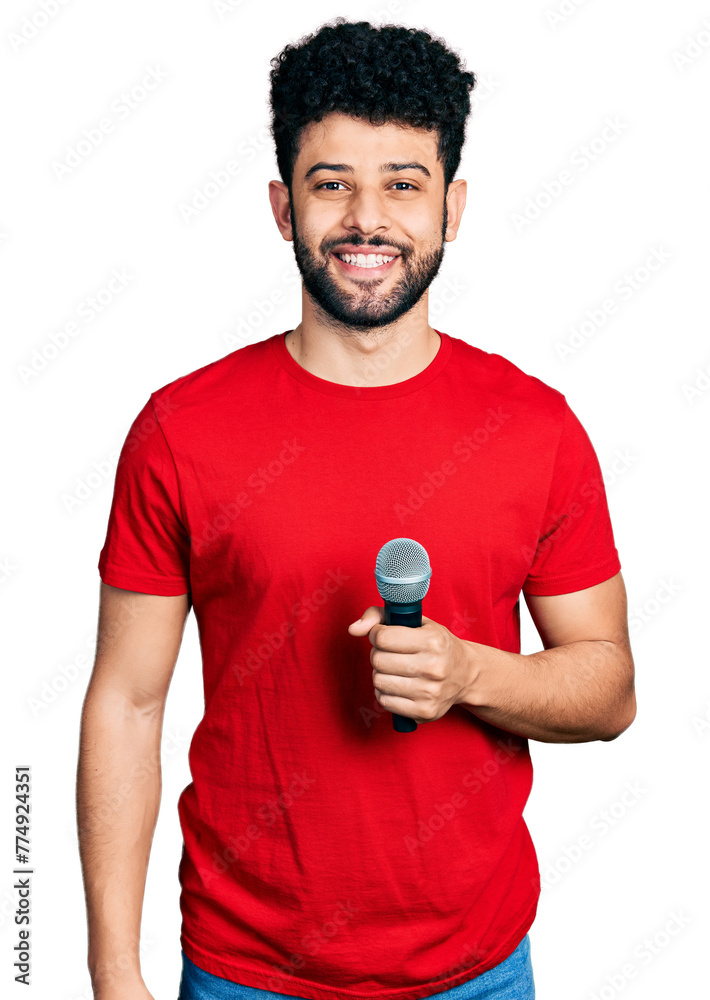 Young arab man with beard singing song using microphone looking positive and happy standing and smiling with a confident smile showing teeth Young arab man with beard singing song using microphone looking positive and happy standing and smiling with a confident smile showing teeth