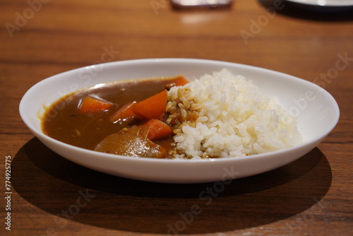 Japanese curry with rice in a white plate on a wooden table © hyungmin
