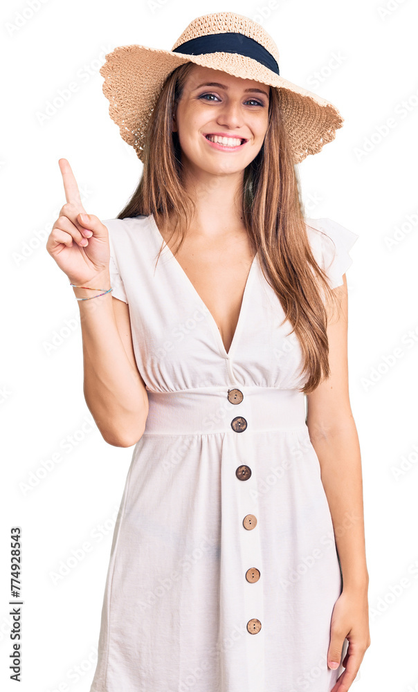 Young beautiful blonde woman wearing summer dress and hat showing and pointing up with finger number one while smiling confident and happy. Young beautiful blonde woman wearing summer dress and hat showing and pointing up with finger number one while smiling confident and happy.