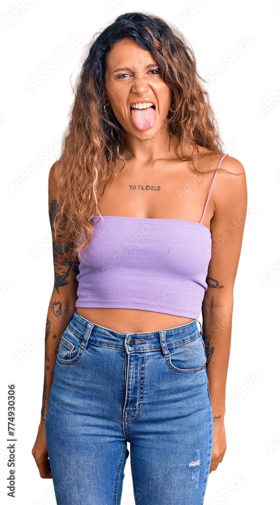 Young hispanic woman with tattoo wearing casual clothes sticking tongue out happy with funny expression. emotion concept. Young hispanic woman with tattoo wearing casual clothes sticking tongue out happy with funny expression. emotion concept.