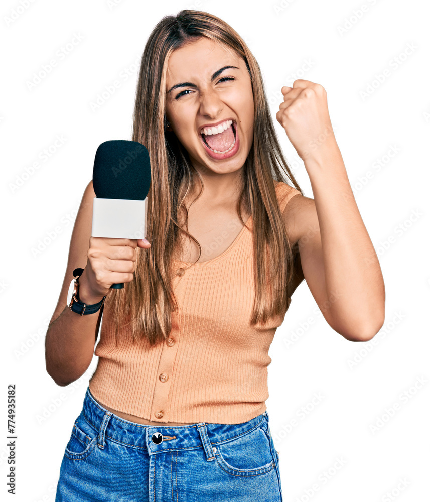 Hispanic young woman holding reporter microphone screaming proud, celebrating victory and success very excited with raised arms