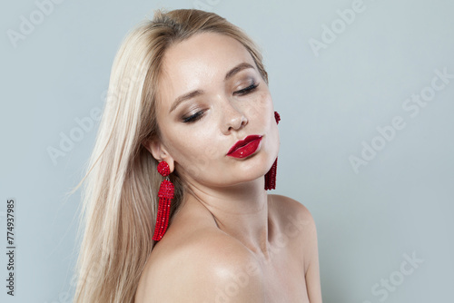 Pretty young woman with make-up and long blonde hair against white studio wall background