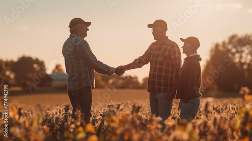 Three generations of farmers shaking hands in warm, glowing field during sunset, depicting family business