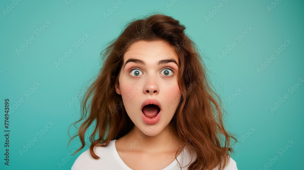 Surprised young woman looking at camera with open mouth, isolated on teal color background professional photography