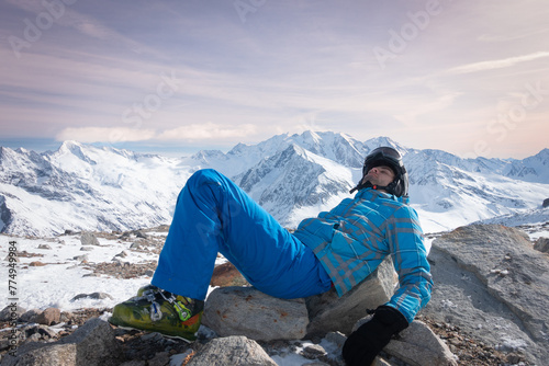  Skier relaxing, resting, laying on rocks,  at sunny day on winter season with beautiful rose sky