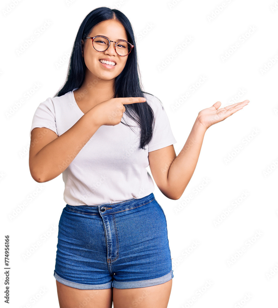 Young beautiful asian girl wearing casual clothes and glasses amazed and smiling to the camera while presenting with hand and pointing with finger. Young beautiful asian girl wearing casual clothes and glasses amazed and smiling to the camera while presenting with hand and pointing with finger.