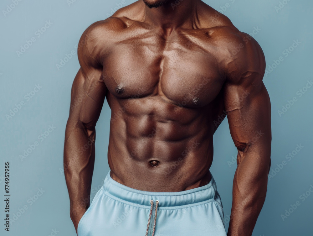 Torso di modello fitness afroamericano in pantaloncini blu chiaro con muscoli addominali ben definiti, sfondo tono su tono turchese , sport