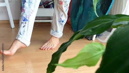 Female artist changing into working clothes, preparing herself to start creating. Painter pull on trouser legs spattered with colorful red and blue paint. High quality 2K footage