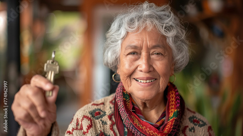 
Happy retired elderly Latin woman showing keys from new home, smiling, promoting mortgage, rent apartment agency service, real estate property buying, photo