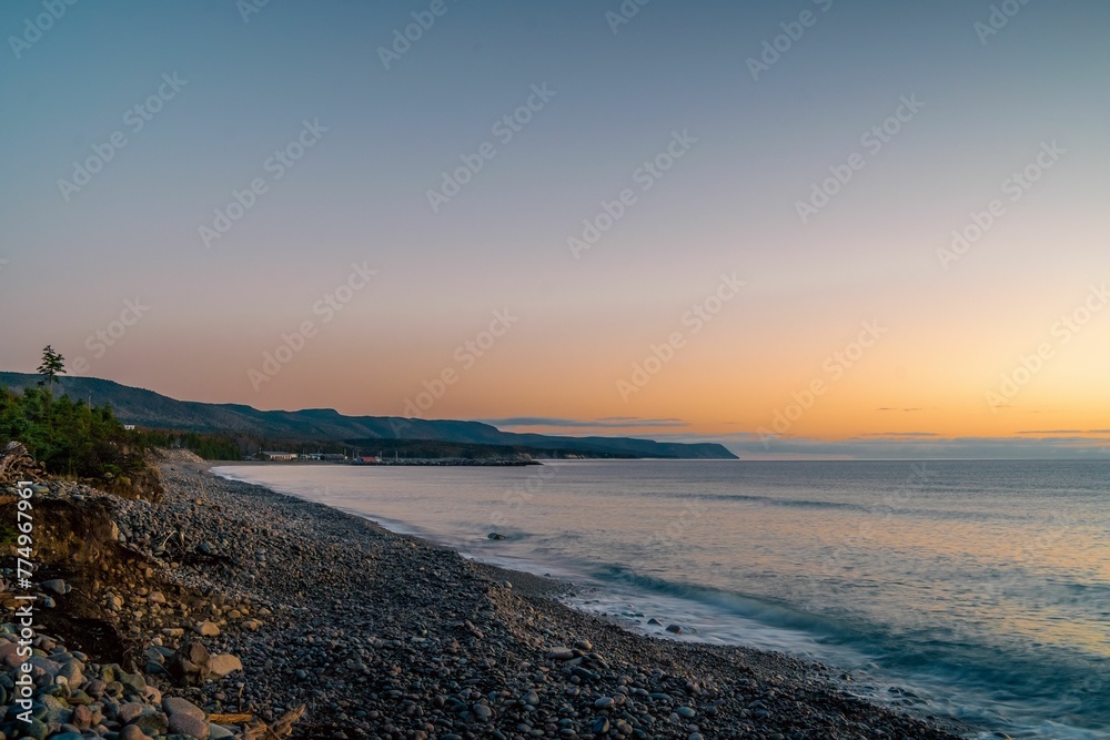 Scenic shot of stones on the coastline of a turquoise sea under the blue sky at sunset Scenic shot of stones on the coastline of a turquoise sea under the blue sky at sunset