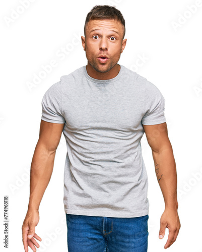 Handsome muscle man wearing casual grey tshirt scared and amazed with open mouth for surprise, disbelief face