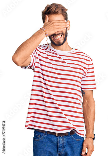 Handsome blond man with beard wearing casual clothes and glasses smiling and laughing with hand on face covering eyes for surprise. blind concept.